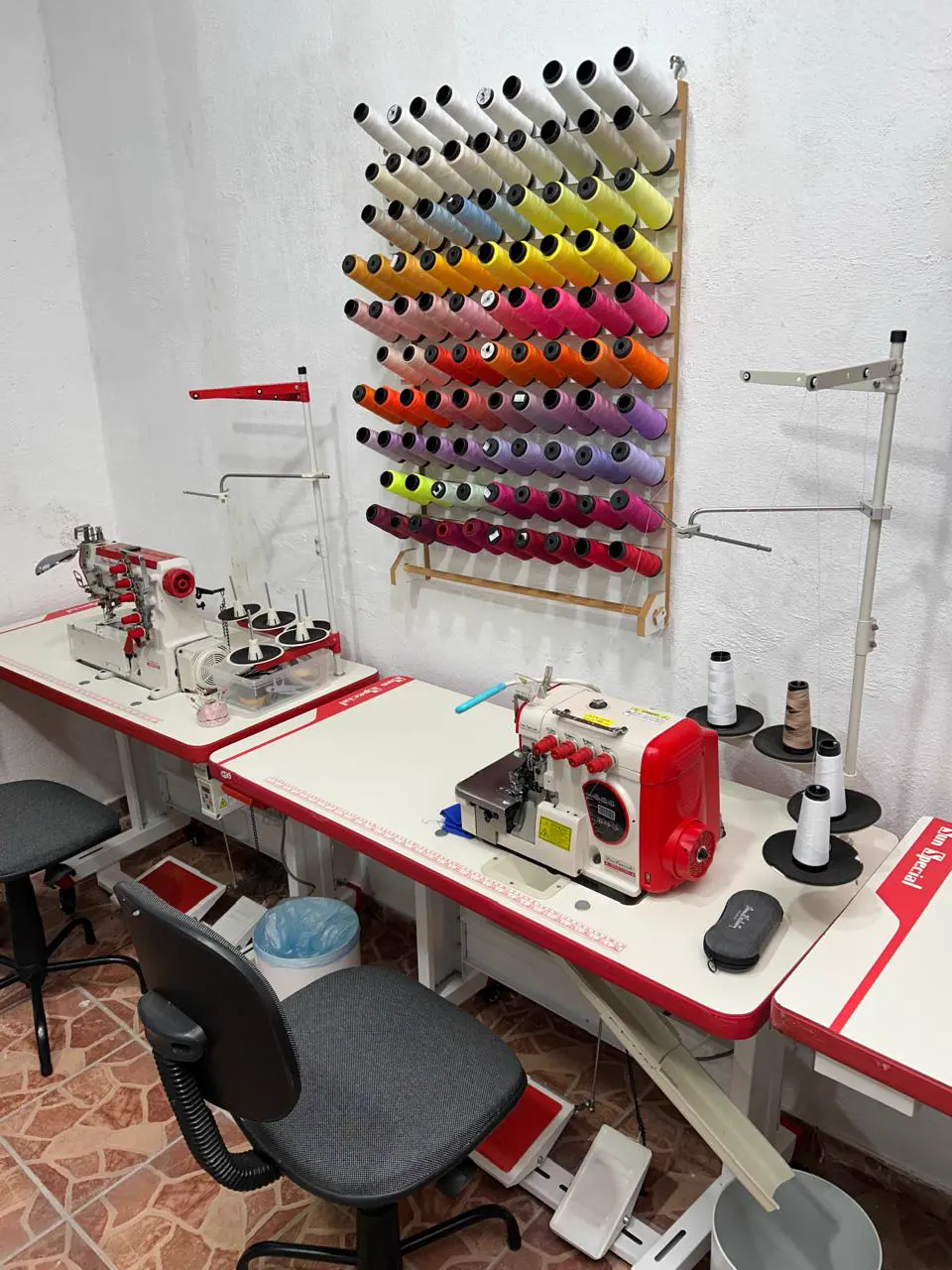 Máquina overloque vermelha em frente à parede de linhas coloridas do ateliê